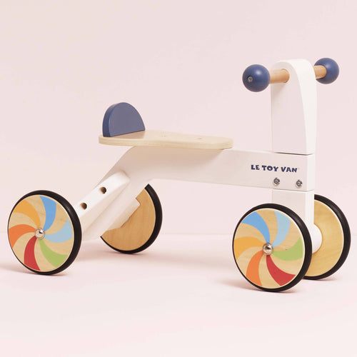 White and dark blue wooden trike ride on toy by Le Toy Van with colourful windmill wheels, designed for toddlers to develop balance and coordination.
