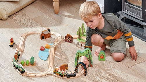 Child playing with a wooden toy train set on a wooden floor.