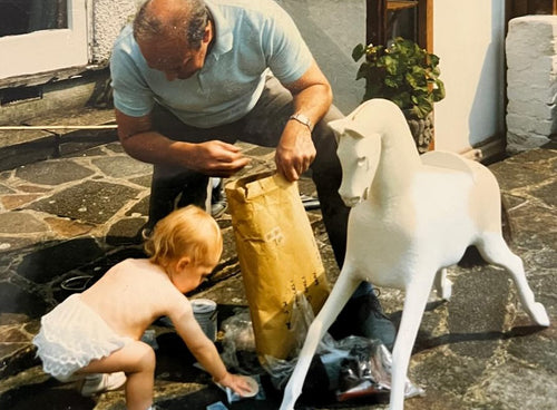 Man and child with a rocking horse being repainted on a stone patio